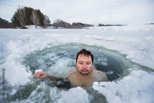 Young man swimming in the winter lake in the ice hole © Dudarev Mikhail