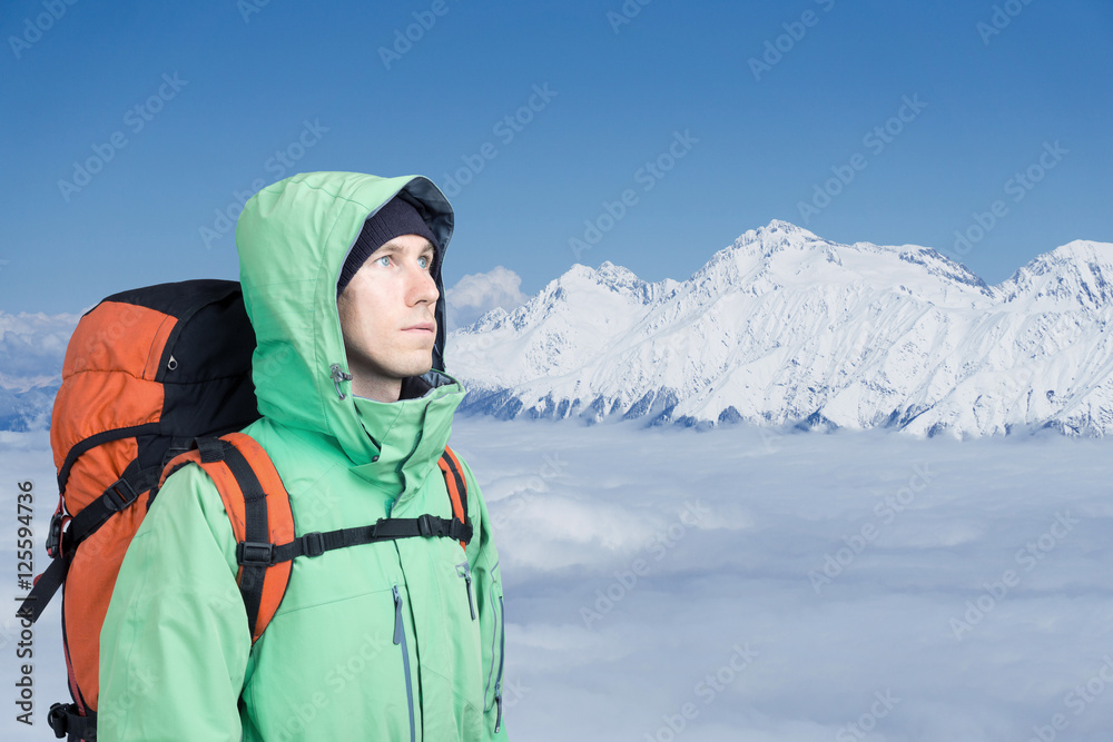 The mountaineer looks at the peak, standing against a winter mountain landscape.