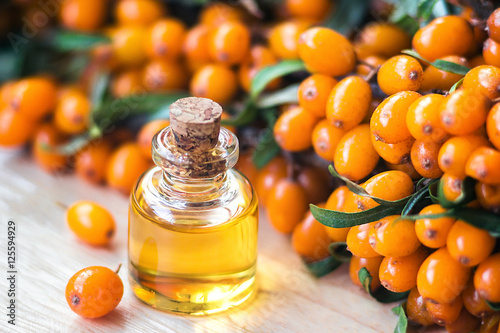 Essential oil of sea buckthorn (Hippophae) in glass bottle with fresh, juicy ripe yellow berries on the branch with green leaves-beauty treatment. Spa concept. Selective focus. photo