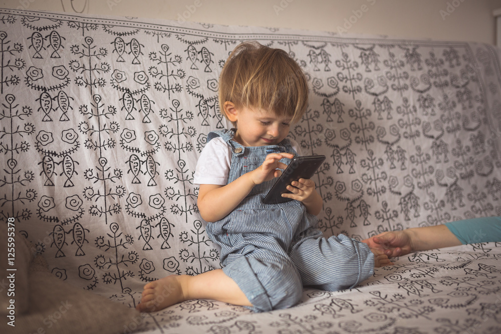 Naklejka premium Toddler boy playing with phone, in light room lifestyle, real in