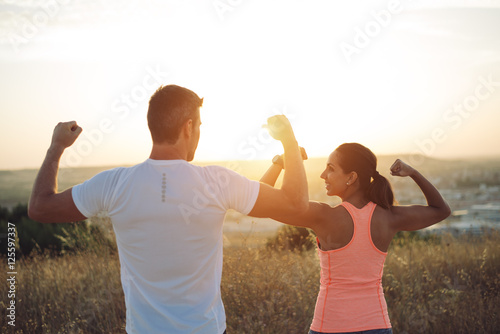 Couple of athletes flexing biceps towards the sunset. Couple of athletes celebrating running outdoor workout success.