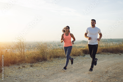 Two athletes running at sunset. Man and woman training together.