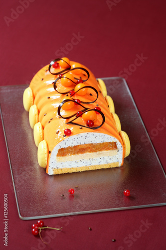 Tableau sur toile Contemporary Yule Log (layered) Cake covered with orange glaze and decorated with french macarons and chocolate loops, on burgundy background