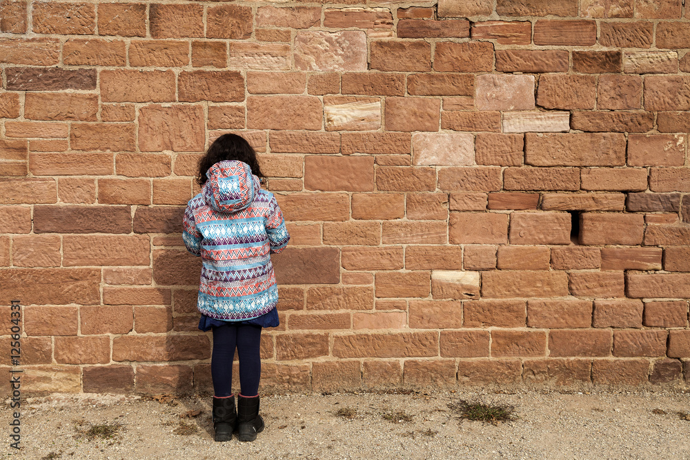 Ein kleines Mädchen steht mit dem Gesicht zur Wand