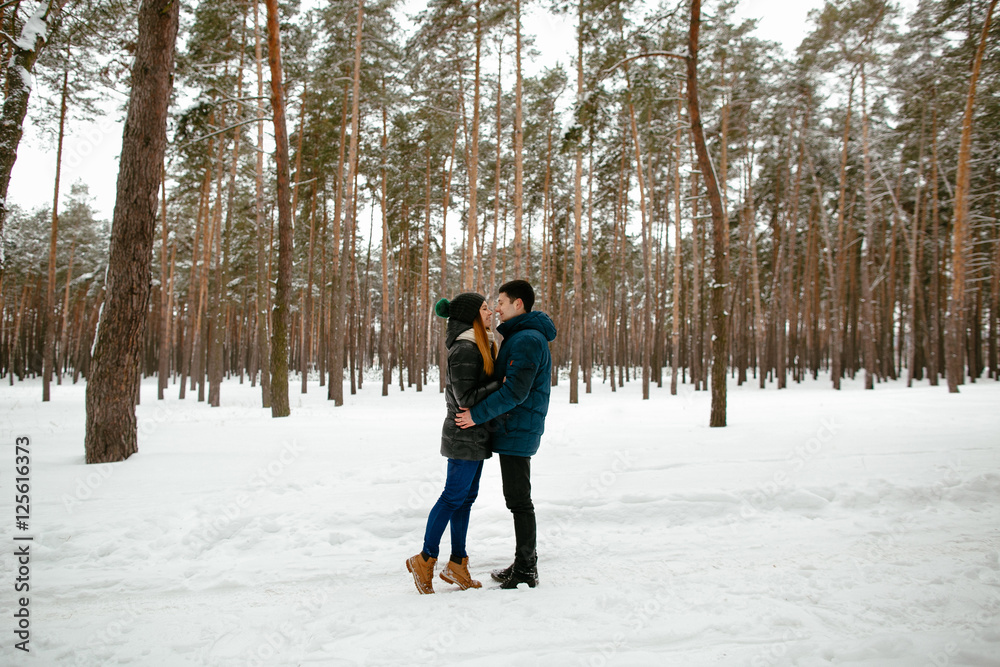 Young couple in warm winter clothing walking in snow-covered forest. Winter