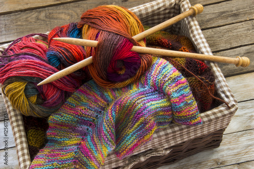 Colorful skeins of wool and wood needles in knitting basket on wooden table