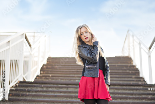 A blonde woman in a red skirt and a black jacket on the stairs
