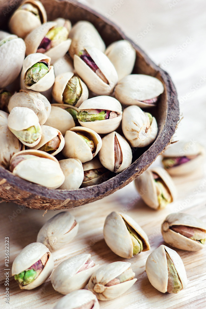 Pistachios in a wooden bowl on light background. Selective focus
