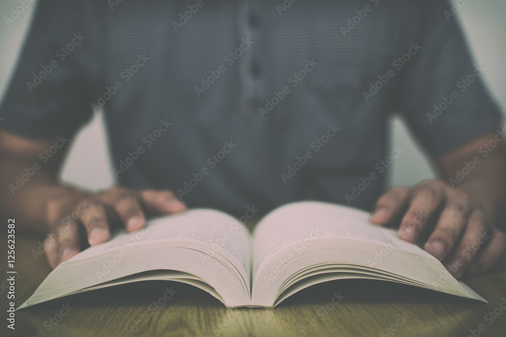 A man reading a book on wooden table with vintage filter blurred background A man reading a book on wooden table with vintage filter blurred background