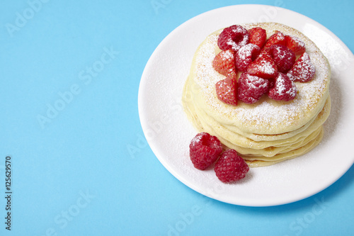 A stack of berry covered pancakes on a bright blue background with blank space at side