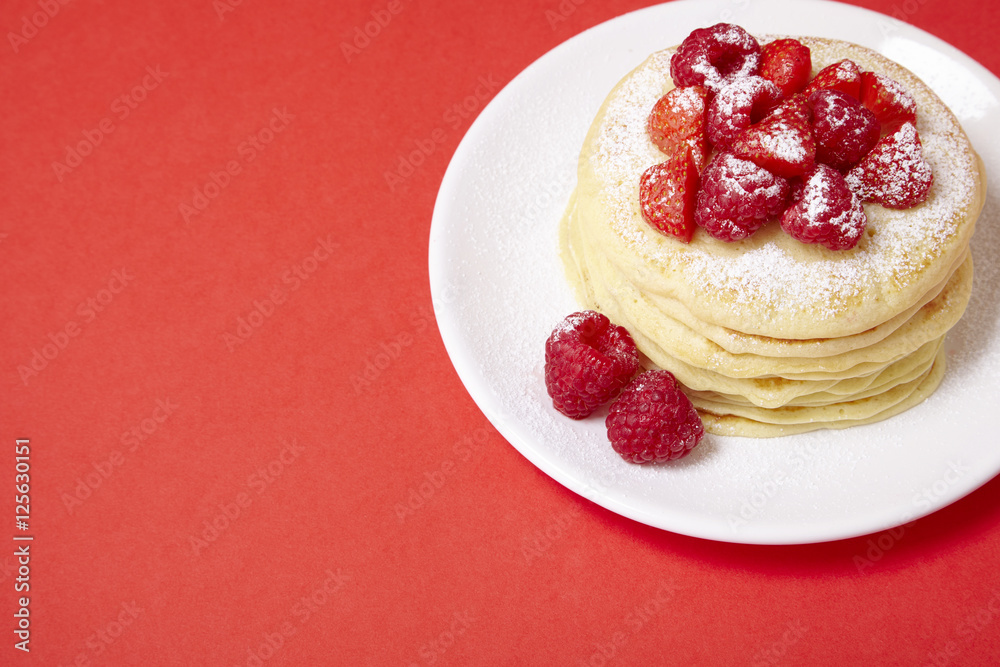A stack of berry covered pancakes on a bright red background with blank space at side A stack of berry covered pancakes on a bright red background with blank space at side