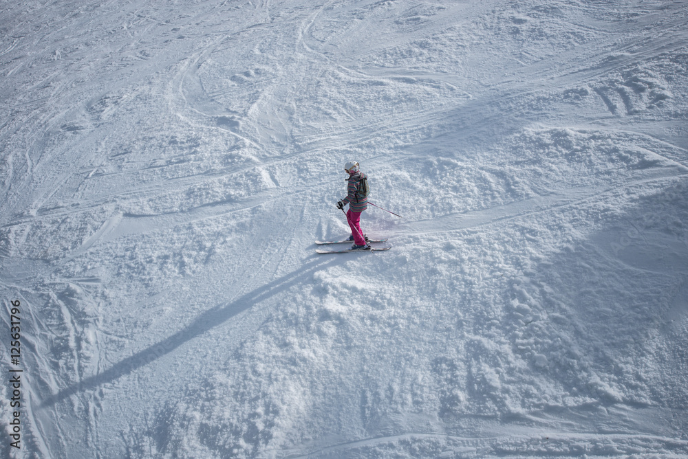 Young girl in colorful outfit skiing downhill on mountain.