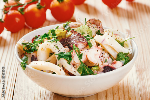 Seafood salad in white bowl, cherry tomato in the background