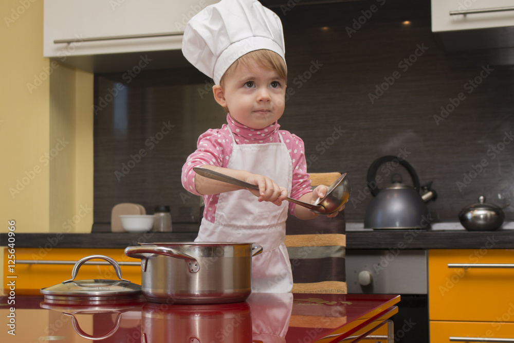 little cute girl in chef suit playing in the kitchen with a ladle and saucepan little cute girl in chef suit playing in the kitchen with a ladle and saucepan