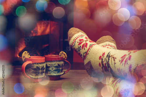 Feet in woollen socks by the Christmas fireplace. Woman relaxes photo