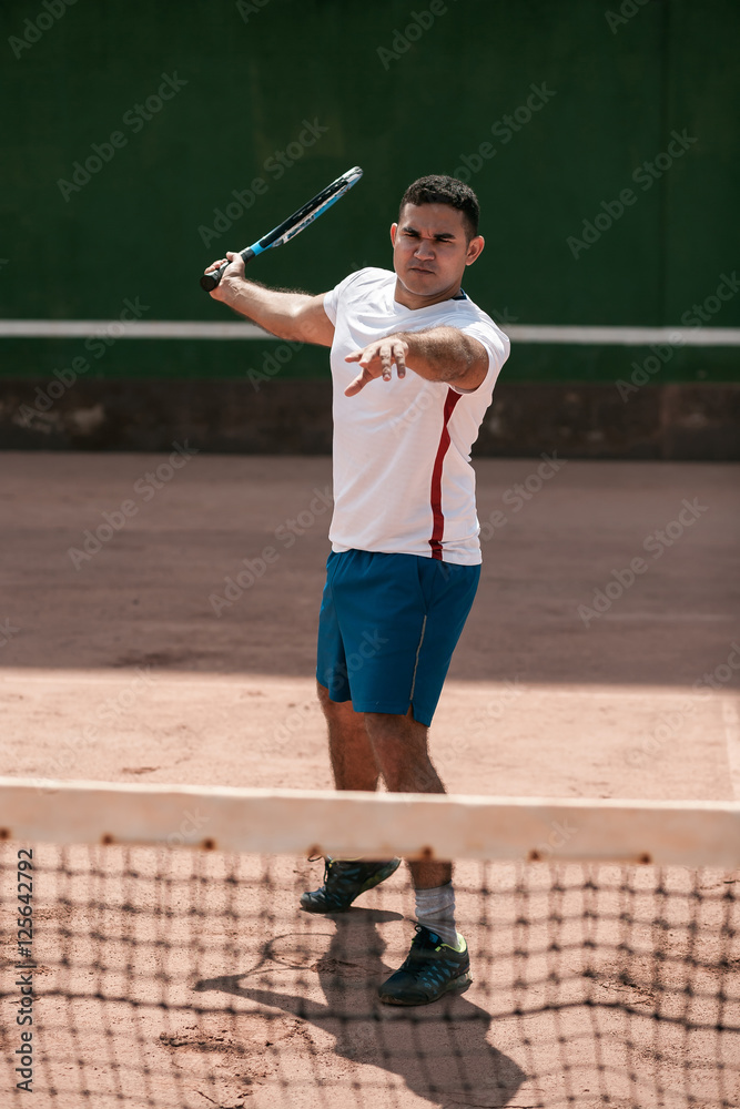 Handsome young man on tennis court. Man playing tennis. Man hitting tennis ball