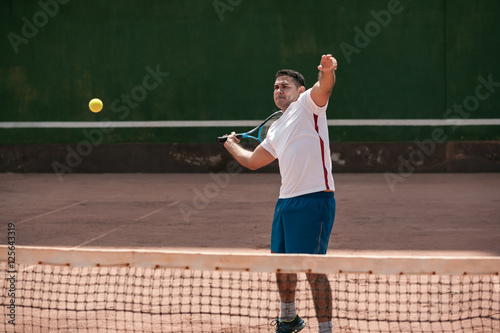Handsome young man on tennis court. Man playing tennis. Man hitting tennis ball © kleberpicui