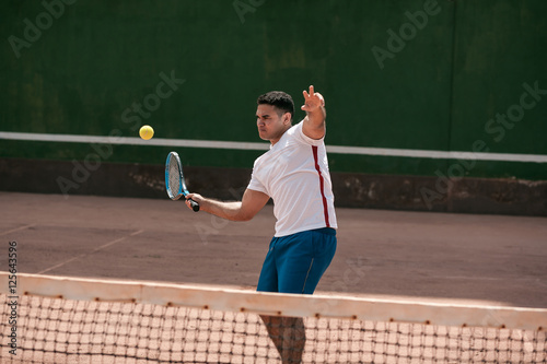 Handsome young man on tennis court. Man playing tennis. Man hitting tennis ball © kleberpicui