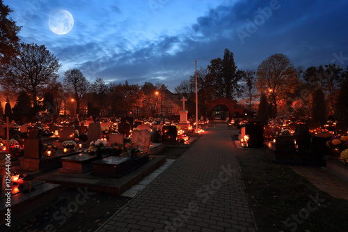 Cmentarz nocą z kolorowymi świecami w Dniu Wszystkich Świętych, księżyc.