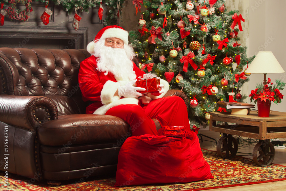 Santa Claus with giftbox on background of sparkling firtree. Christmas