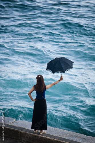Woman seen from behind holding a blue umbrella watching the sea