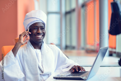 Sudanese business man in traditional outfit using mobile phone in office