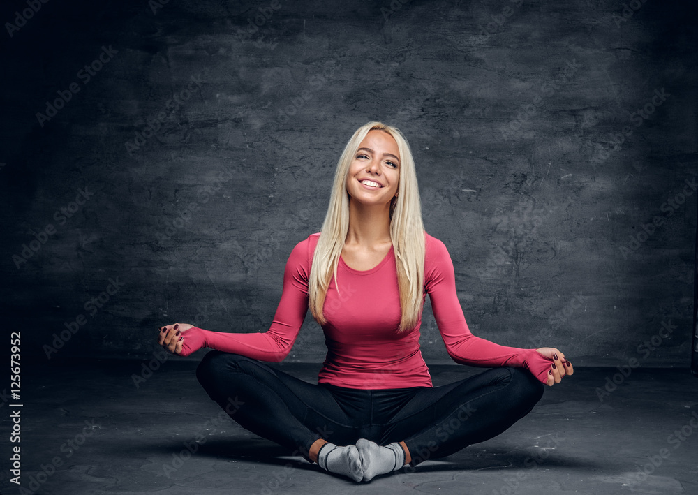 Fototapeta premium Blonde girl sits on a floor in a studio over grey background.
