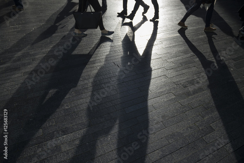 Shadows of pedestrians make an abstract background on a modern shiny surface backlit by bright contrasting sun