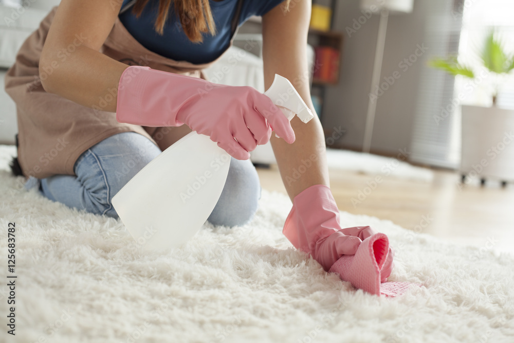 Young woman cleaning carpet in room