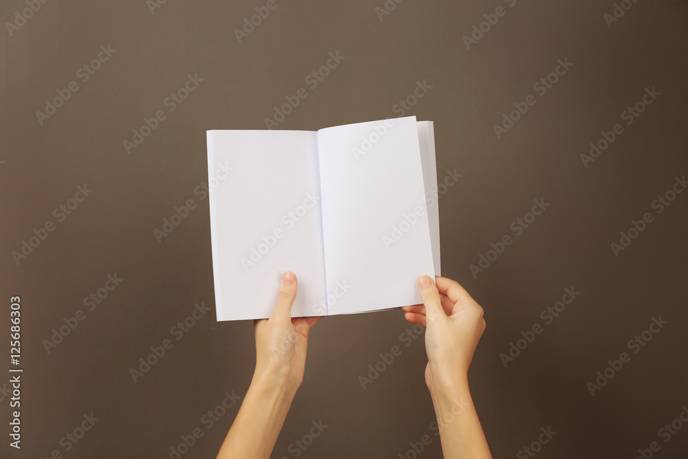 Female hands holding blank open brochure on grey background Female hands holding blank open brochure on grey background