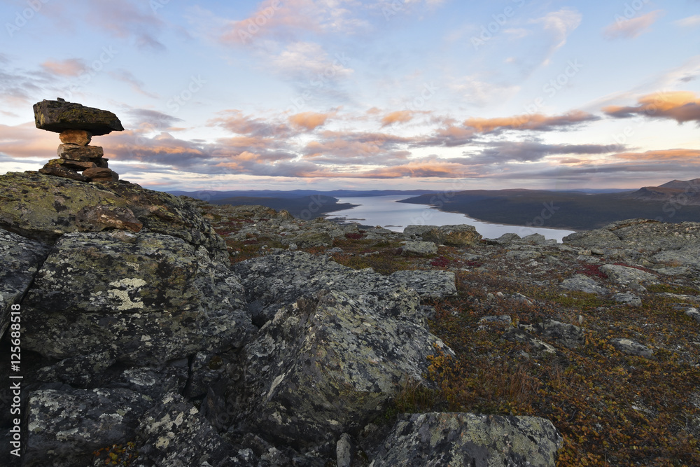 Fototapeta premium Pile of stones marks the mountain top, beautiful sunset and lake background