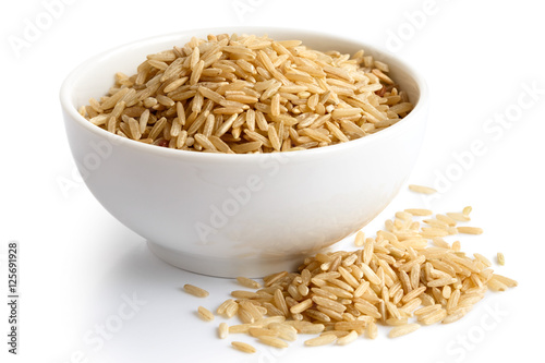 Bowl of long grain brown rice isolated on white. Spilled rice.