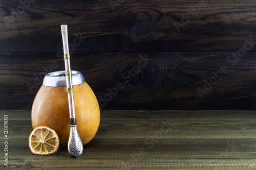 Yerba mate in gourd matero with bombila and lemon slice on wooden background. photo