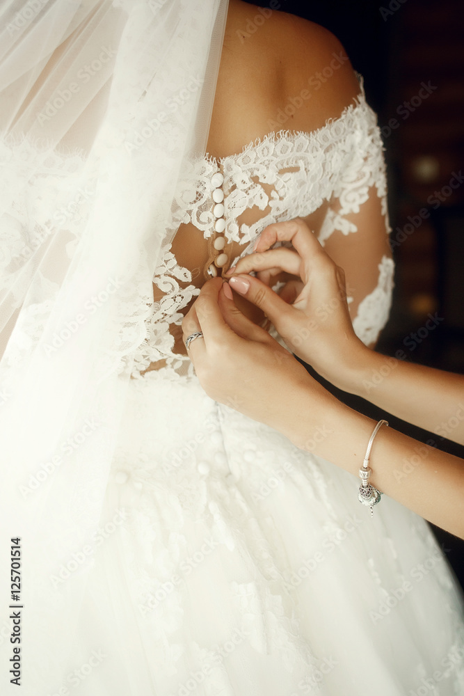 Bridesmaid adjusts wedding dress on bride's back