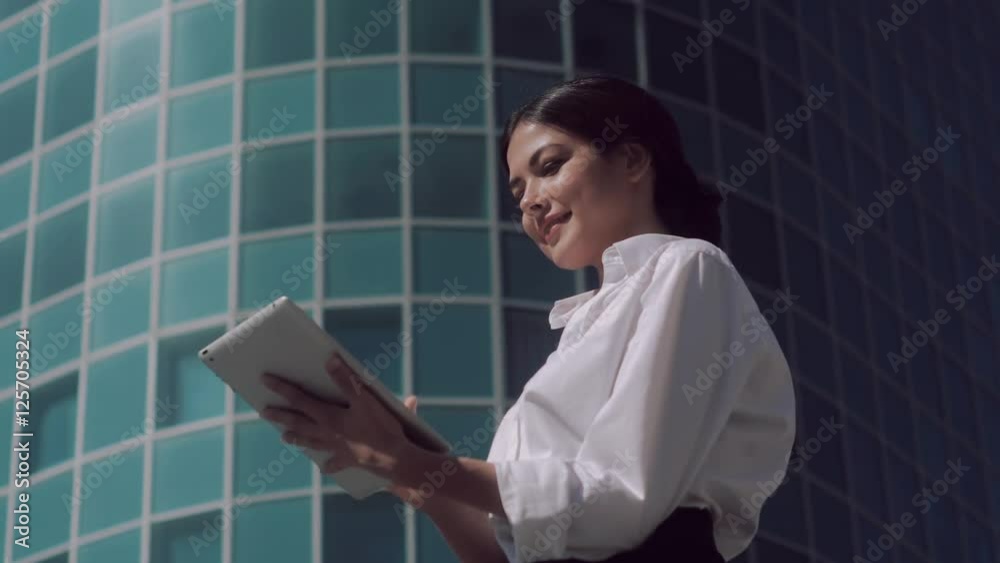 Smiling business woman standing outdoors on a sunny day and working on her tablet
