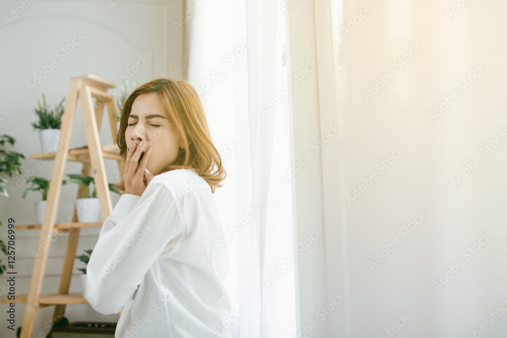 Tired sleepy Asia woman yawning and holding a cup of coffee, overwork and sleep deprivation concept,flare light