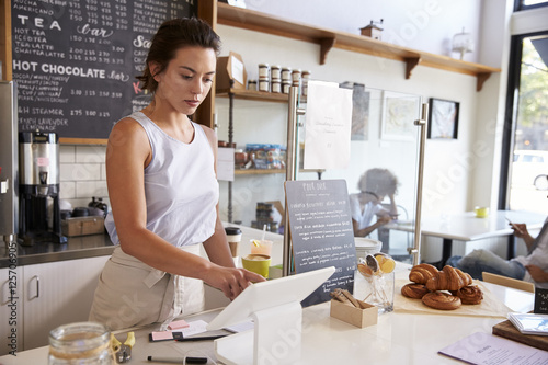 Woman working on the till at a coffee shop, wide angle