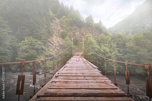 Fototapeta Naklejka Na Ścianę i Meble -  Подвесной деревянный мост в тумане над горной рекой в Сванетии, Грузия.