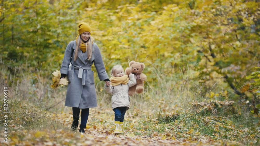 Little daughter with her mommy and Taddy bear walks in autumn park - plays the leaves Little daughter with her mommy and Taddy bear walks in autumn park - plays the leaves