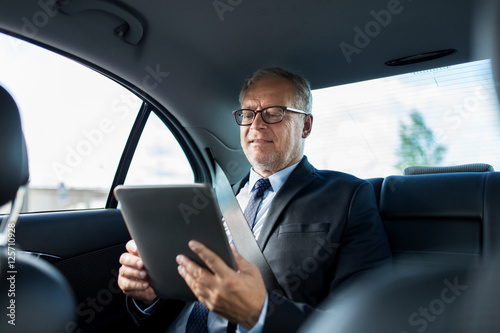 senior businessman with tablet pc driving in car