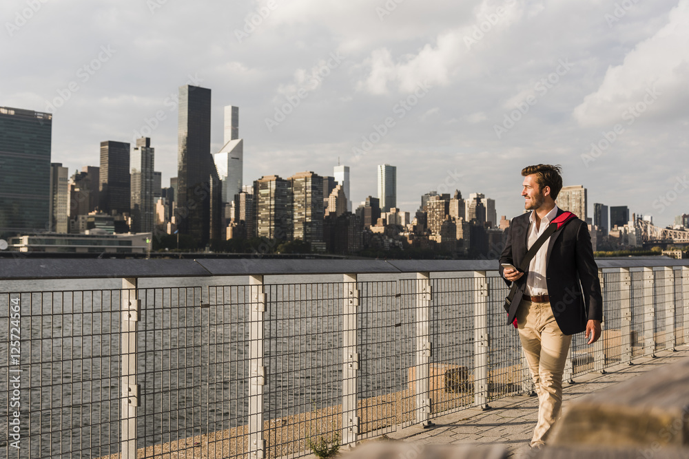USA, New York City, businessman walking along East River USA, New York City, businessman walking along East River