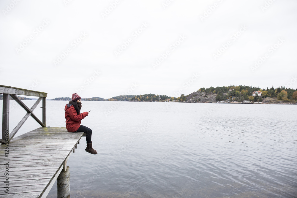 Woman sitting on pier text messaging Woman sitting on pier text messaging