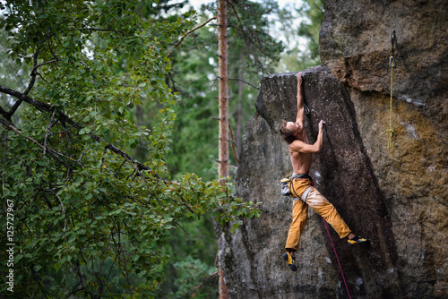Extreme sport climbing. Young male rock climber reaching the top of a rock.
