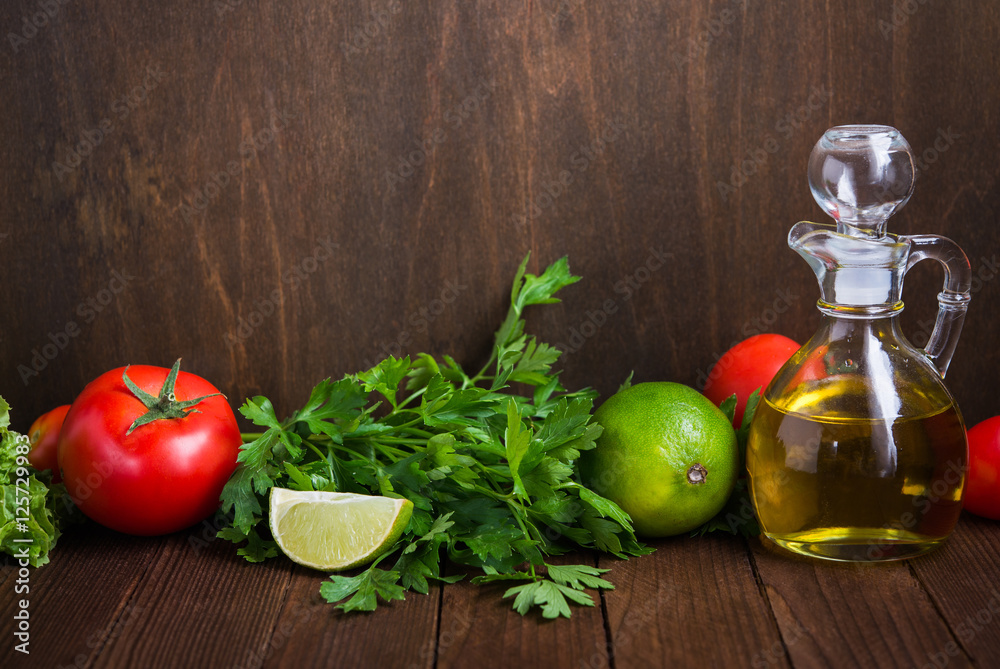 Fresh tomatoes, lime, lettuce, parsley and olive oil on dark wood background with space for text. Healthy food. Vegetables and greens. Salad ingredients.