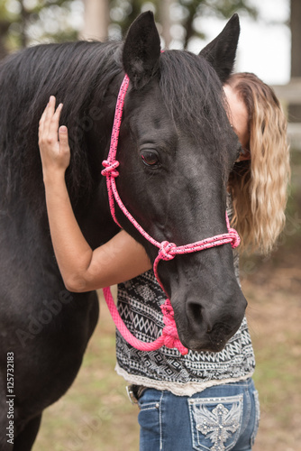 Blonde woman giving a black horse a hug