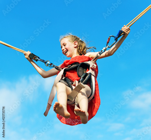 Foto Little girl on bungee trampoline with cords. Place for text.