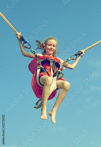 Canvas Print Little girl on bungee trampoline with cords. Place for text.