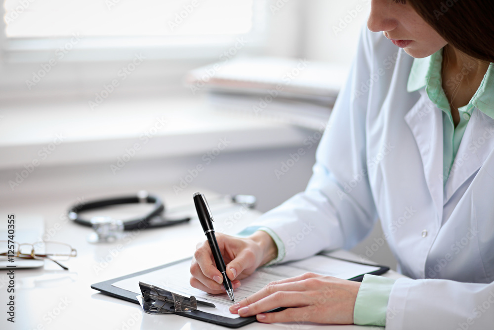 Close up of unknown female doctor sitting at the table near the window in hospital and typing at laptop computer Close up of unknown female doctor sitting at the table near the window in hospital and typing at laptop computer