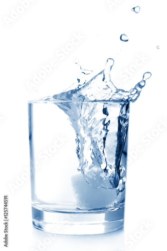 Ice in glass of water with splash on white background .