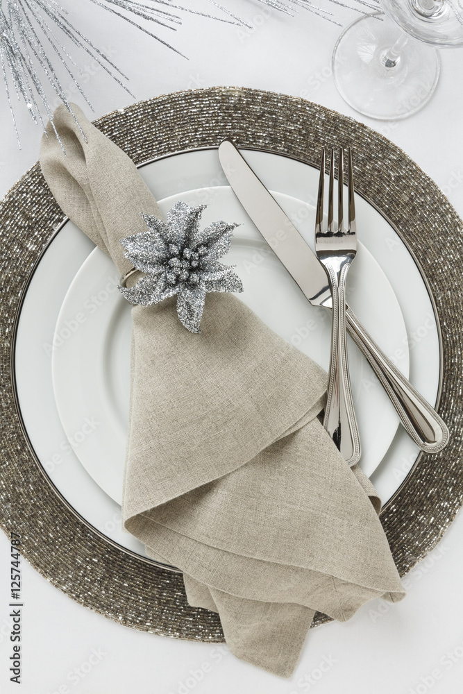 Festive fancy formal fine dining Christmas or New Year's Eve holiday dinner  party table setting place setting with white china plates, silverware,  linen cloth napkin and silver glitter decorations foto de Stock